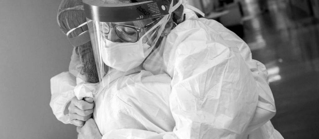 two medical frontliners wearing protective equipment hugging each other